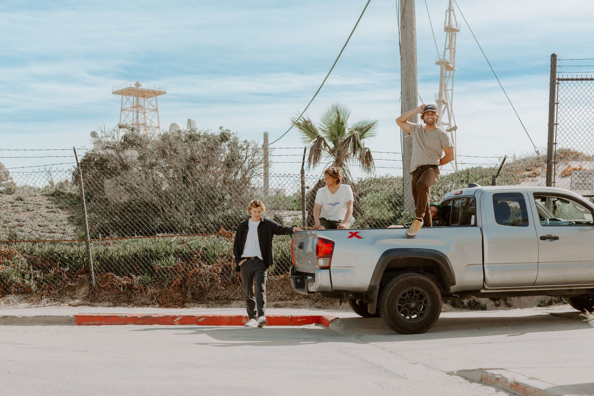 Friends hanging out on and around a silver pickup truck by the coast, wearing Daily belts